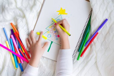 Çocuk renkli kalem ve marker ile bir Noel ağacı çizer