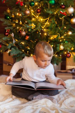 Çocuk Noel ağacının altındaki kitaba bakıyor..