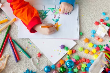 Bir çocuk Noel ağacını çizer. Çocuk Noel 'ı çiziyor. Çocuk katta yatıyor ve beyaz kağıt ile bir defter berabere.