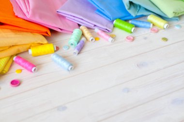 Renkli kumaş katlanmış yığını. İğne yatak, makas, ölçüm bandı. Bej renkli arka plan.