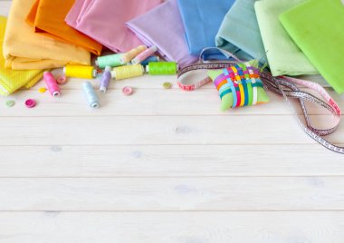 Renkli kumaş katlanmış yığını. İğne yatak, makas, ölçüm bandı. Bej renkli arka plan.