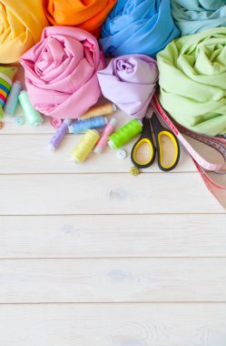 Renkli kumaş katlanmış yığını. İğne yatak, makas, ölçüm bandı. Bej renkli arka plan.