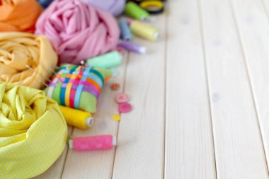 Renkli kumaş katlanmış yığını. İğne yatak, makas, ölçüm bandı. Bej renkli arka plan.