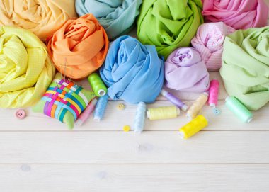 Renkli kumaş gül çiçek şeklinde katlanmış. Makas, bant ölçü, iğne, iğne mili, düğmeleri.