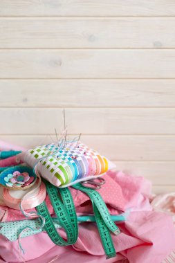 Dikiş aksesuarları beyaz bir arka plan üzerinde yalan. Ölçüm bandı, iplik, kumaş ve Dikiş iğneler. Kumaş pembe, nane ve turkuaz.