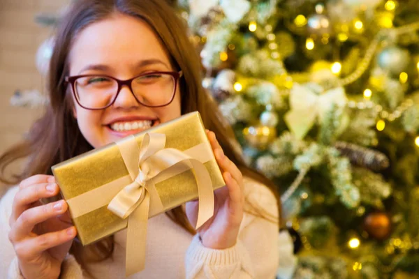 Het meisje houdt in haar handen en opent een gouden kerstcadeau. L — Stockfoto