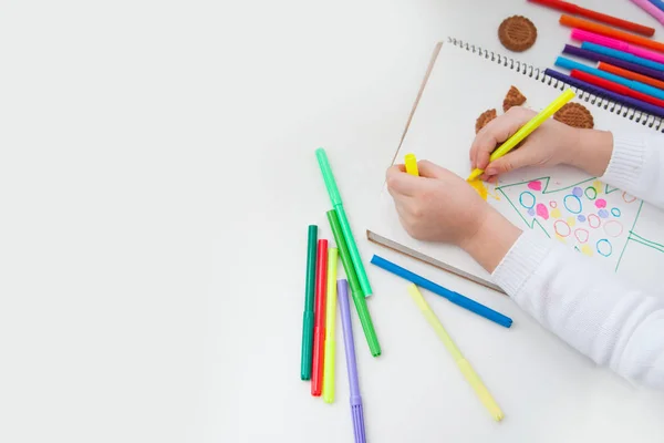 The child draws Christmas pencils in a notebook.