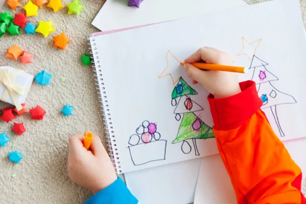 男の子がクリスマスツリーを描きます 子供のドローイング クリスマス子供は床に横たわって 白い紙でノートを描きます — ストック写真