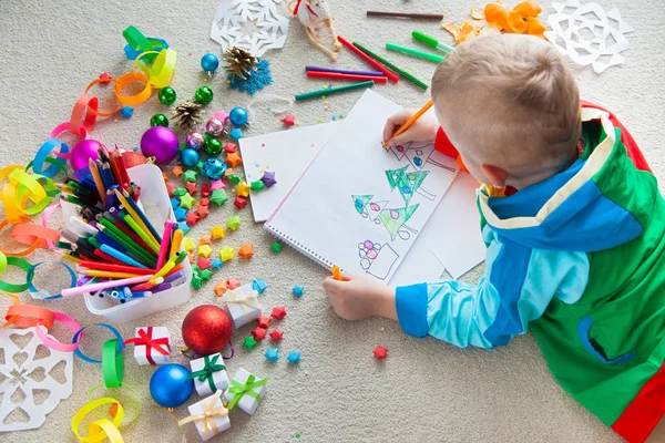 The child draws a Christmas tree with markers and colored pencil