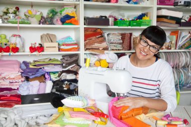 Bir dikiş makinesi yanında mutlu gülümseyen kadın. Kumaş, iplik ve makas. Dikiş aksesuarları.