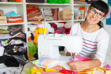 Bir dikiş makinesi yanında mutlu gülümseyen kadın. Kumaş, iplik ve makas. Dikiş aksesuarları.