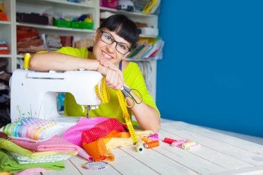 Bir dikiş makinesi yanında mutlu gülümseyen kadın. Kumaş, iplik ve makas. Dikiş aksesuarları.