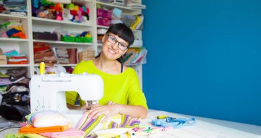 Bir dikiş makinesi yanında mutlu gülümseyen kadın. Kumaş, iplik ve makas. Dikiş aksesuarları.