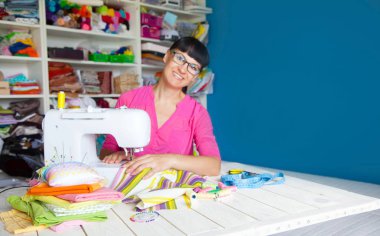 Bir dikiş makinesi yanında mutlu gülümseyen kadın. Kumaş, iplik ve makas. Dikiş aksesuarları.