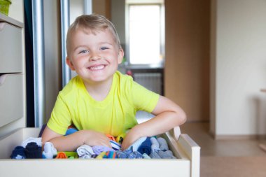 Çocuğun elbiselerini koyar. Çocuk T-shirt dolaptan çeker.