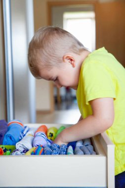 Çocuğun elbiselerini koyar. Çocuk T-shirt dolaptan çeker.