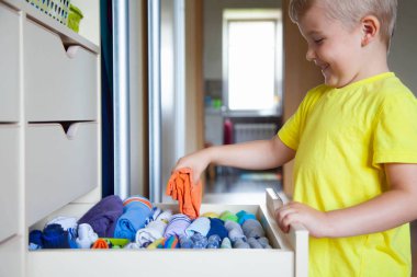 Çocuğun elbiselerini koyar. Çocuk T-shirt dışarı çeker 