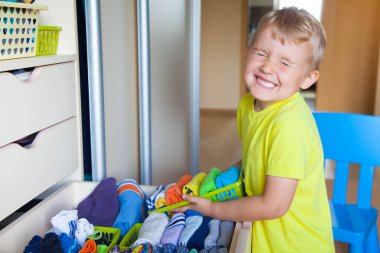 Çocuğun elbiselerini koyar. Çocuk T-shirt dolaptan çeker.