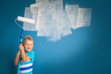 Çocuk bir rulo ile mavi duvar boyar. La çocuk tutar