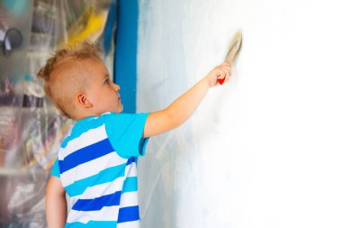 Çocuk bir rulo ile mavi duvar boyar. La çocuk tutar