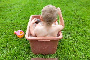 Yeşil çimenlerin üzerinde banyoda küçük çocuk yıkar. 4-5 / çocuk