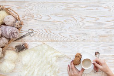 İplik olduğunu bej, kahverengi, gri ve beyaz. Arka plan yaşlı ahşap. İğneler, makas, kahve, örgü, örgü örme kumaş.