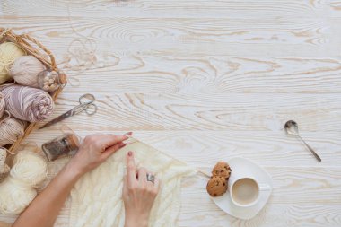 İplik olduğunu bej, kahverengi, gri ve beyaz. Arka plan yaşlı ahşap. İğneler, makas, kahve, örgü, örgü örme kumaş.