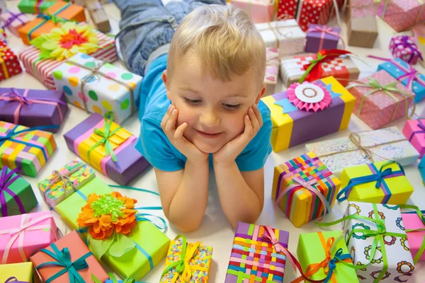 子供にはプレゼントが散らばっています 少年にある床の上 そして彼の周り多くのお祝いギフト ボックス — ストック写真