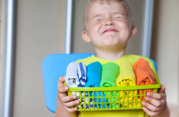 The child keeps his things. The boy puts the T-shirts in a drawer.