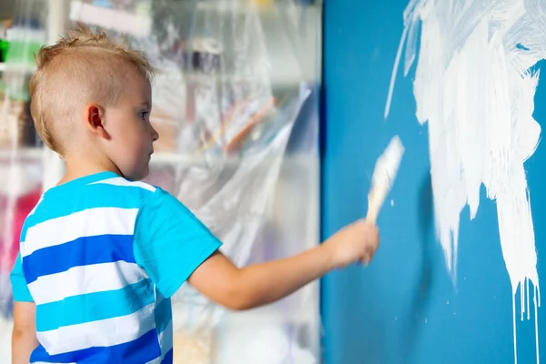 El niño pinta la pared azul con un rodillo. El chico sostiene a la — Foto de Stock