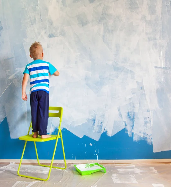 El niño pinta la pared azul con un rodillo. El chico sostiene a la — Foto de Stock