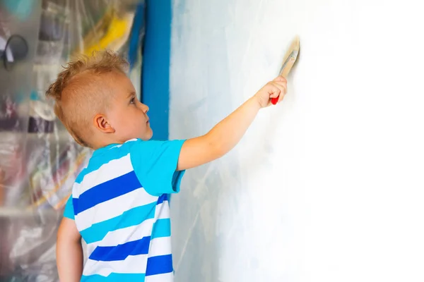 Il bambino dipinge la parete blu con un rullo. Il ragazzo tiene un la — Foto Stock