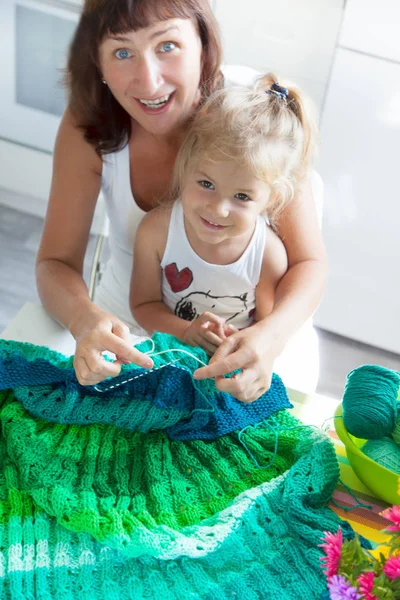 Mom teaches my daughter to knit a green knitted fabric of thick
