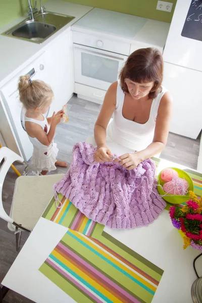 Mamá enseña a mi hija a tejer una tela verde de punto grueso — Foto de Stock