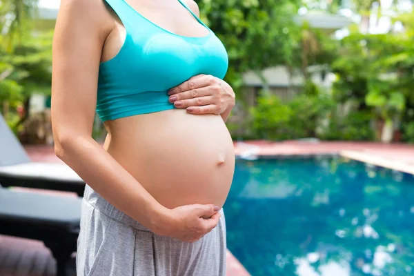 Μια έγκυος γυναίκα στέκεται στα ρούχα της γιόγκα και αγκαλιάζει το στομάχι της. Ne — Φωτογραφία Αρχείου
