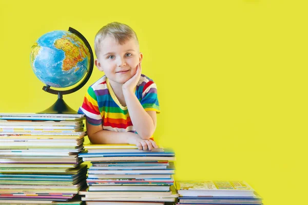 O rapaz senta-se ao lado dos livros infantis e do globo. Verde b — Fotografia de Stock