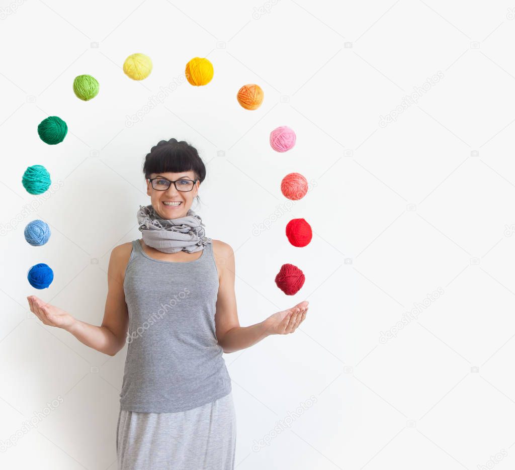 The girl is standing and throwing up the colored balls of yarn.