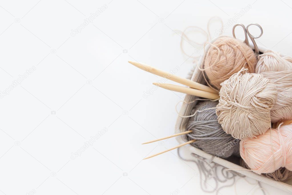 Neutral beige yarn for knitting is in the basket. Knitting needl