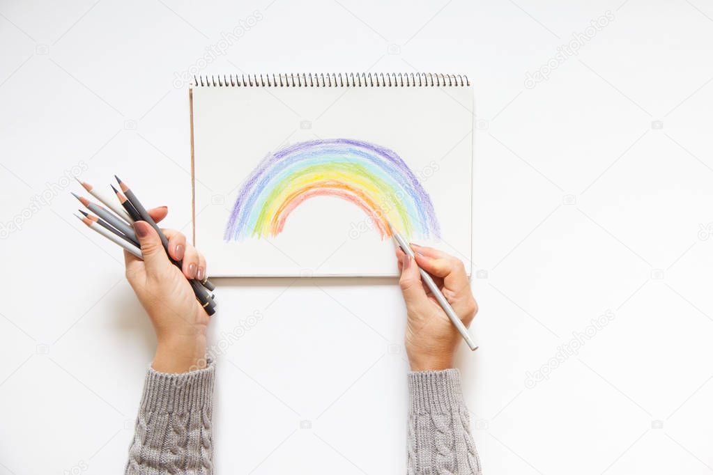 Hand with color pencils and blank sheet of paper. Rainbow.