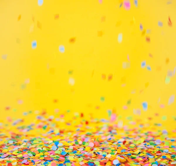 Confete colorido voando sobre fundo amarelo — Fotografia de Stock