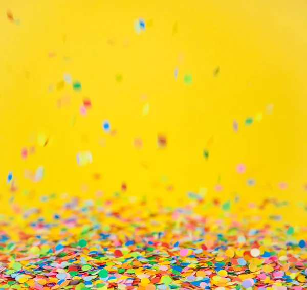 Цветные конфетти летят на желтом фоне — стоковое фото