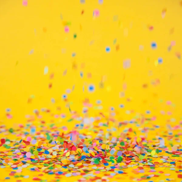 Colored confetti flying on yellow background — Stock Photo, Image