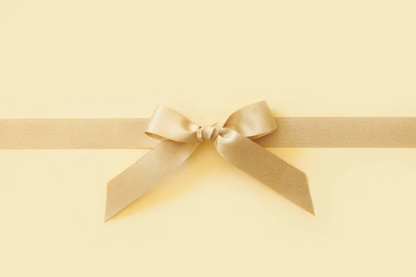ベージュの背景に贈り物として弓を持つ金のリボン — ストック写真