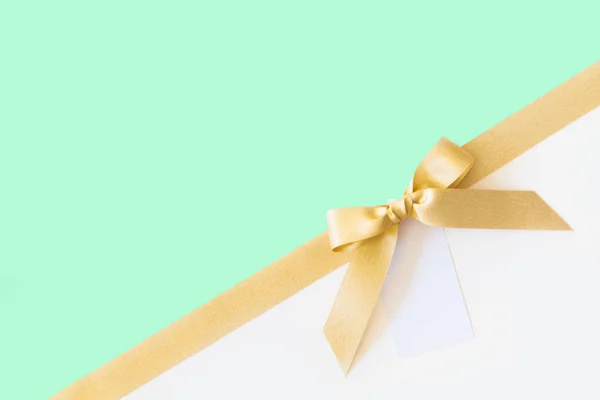 Gold ribbon with a bow as a gift on a white and mint background — Stock Photo, Image