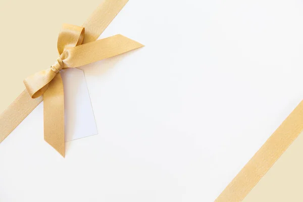 Gold ribbon with a bow as a gift on a white and beige background — Stock Photo, Image