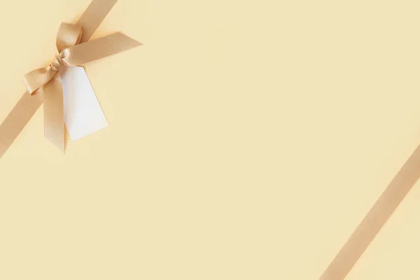 Золотая лента с луком в подарок на бежевом фоне — стоковое фото