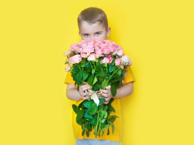 Sarı giyimli bir çocuk elinde büyük bir buket gül tutuyor ve. 