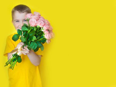 Sarı giyimli bir çocuk elinde büyük bir buket gül tutuyor ve. 