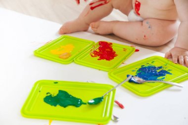 Bebek çocuk renkli boyalar elleri, kirli ayakları ile çizer. Beyaz li