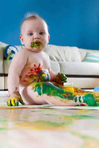 Baby child draws with colored paints hands, dirty feet. White li